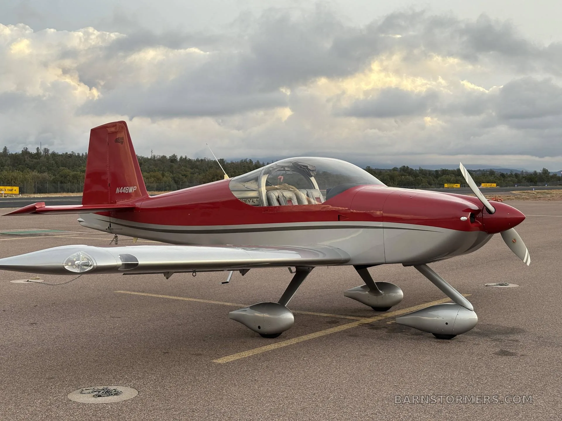 A red and silver single-engine aircraft, N448WP, parked on an asphalt ramp under a cloudy sky.