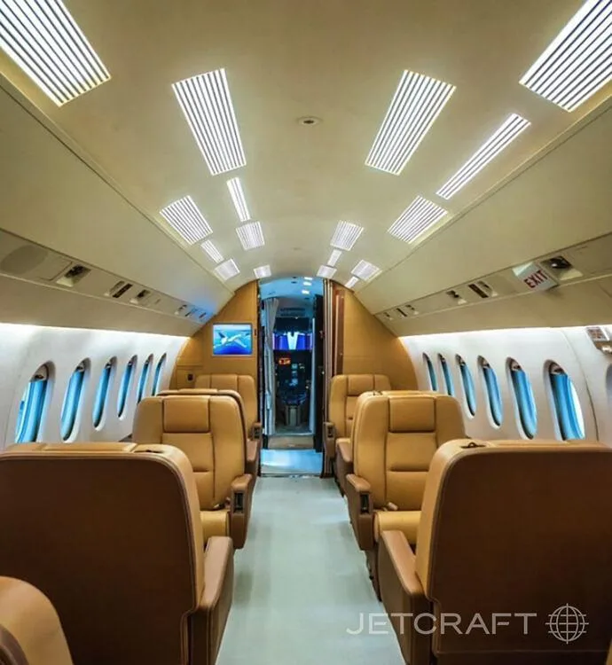A view down the aisle of a business jet cabin with tan leather seats and overhead lighting.