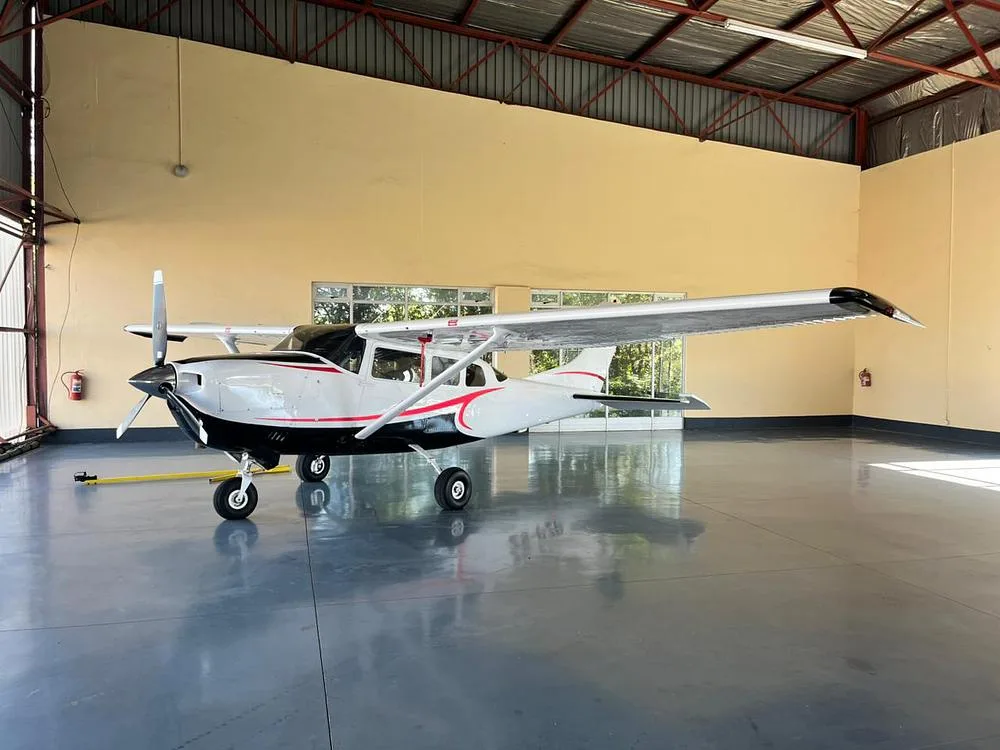 A white and black Cessna aircraft with red stripes is parked inside a hangar.