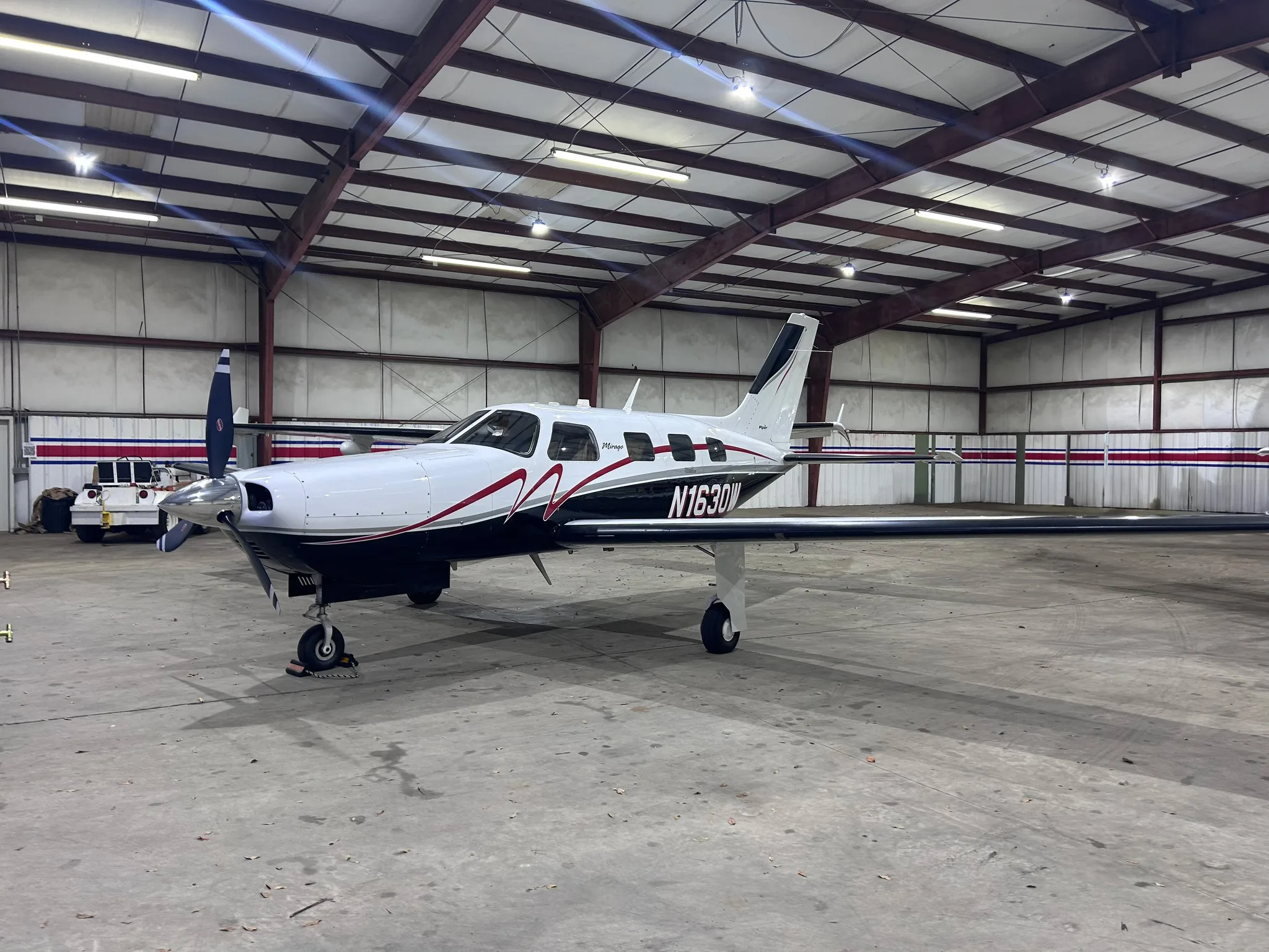 A white and black Piper Mirage aircraft with red accents, registration N1630W, parked inside a hangar.