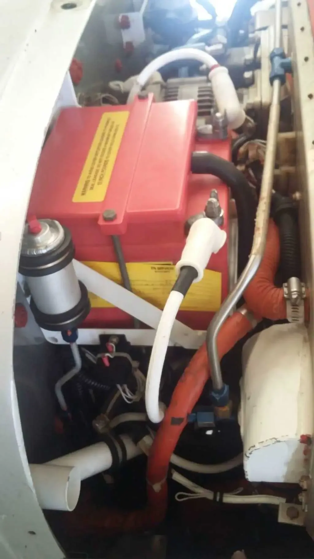 A close-up view of an aircraft's engine compartment showing a red battery, hoses, and wiring.