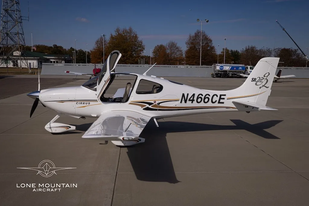 A white Cirrus SR22 aircraft with gold and black stripes, registration N466CE, parked on an airfield with its doors open, viewed from the right side.