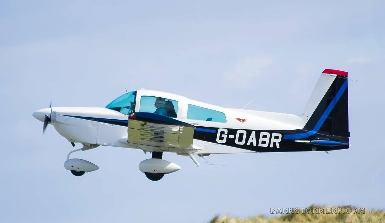 A white and blue light aircraft, registration G-OABR, in flight against a light blue sky.