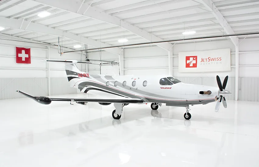 A close-up view of the front fuselage of a white Pilatus PC-12NG aircraft with "PILATUS" in red text and gray and red stripes.
