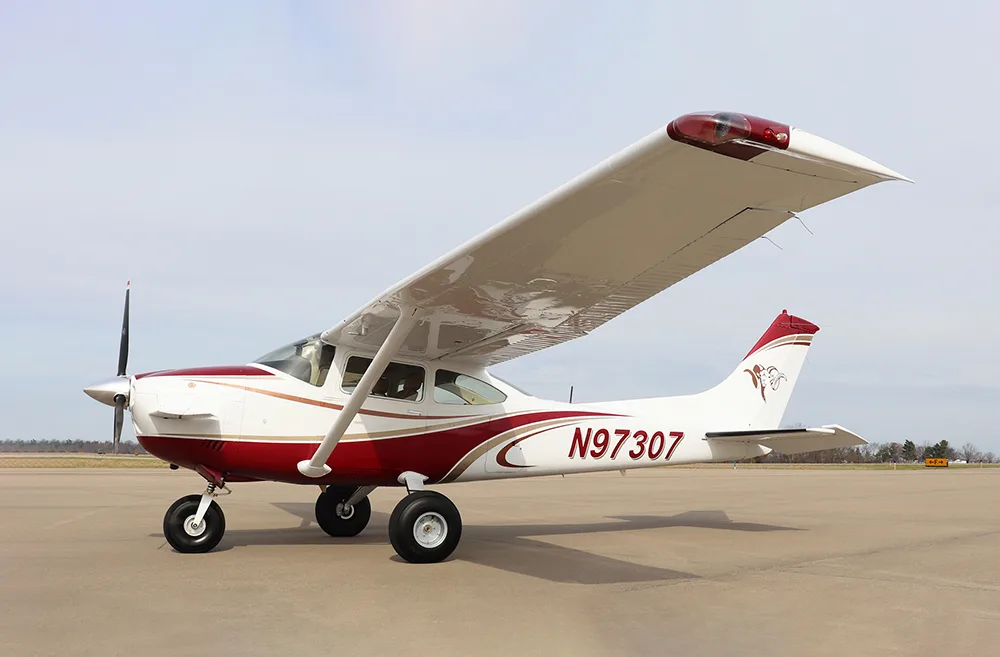 A side view of a white and red single-engine high-wing aircraft, N97307, parked on an airfield.