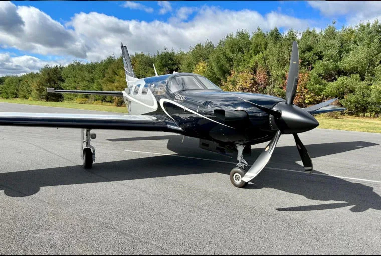 A front-right view of a black and silver Piper M600 SLS aircraft (N63NY) on an airfield, showing the propeller and nose.