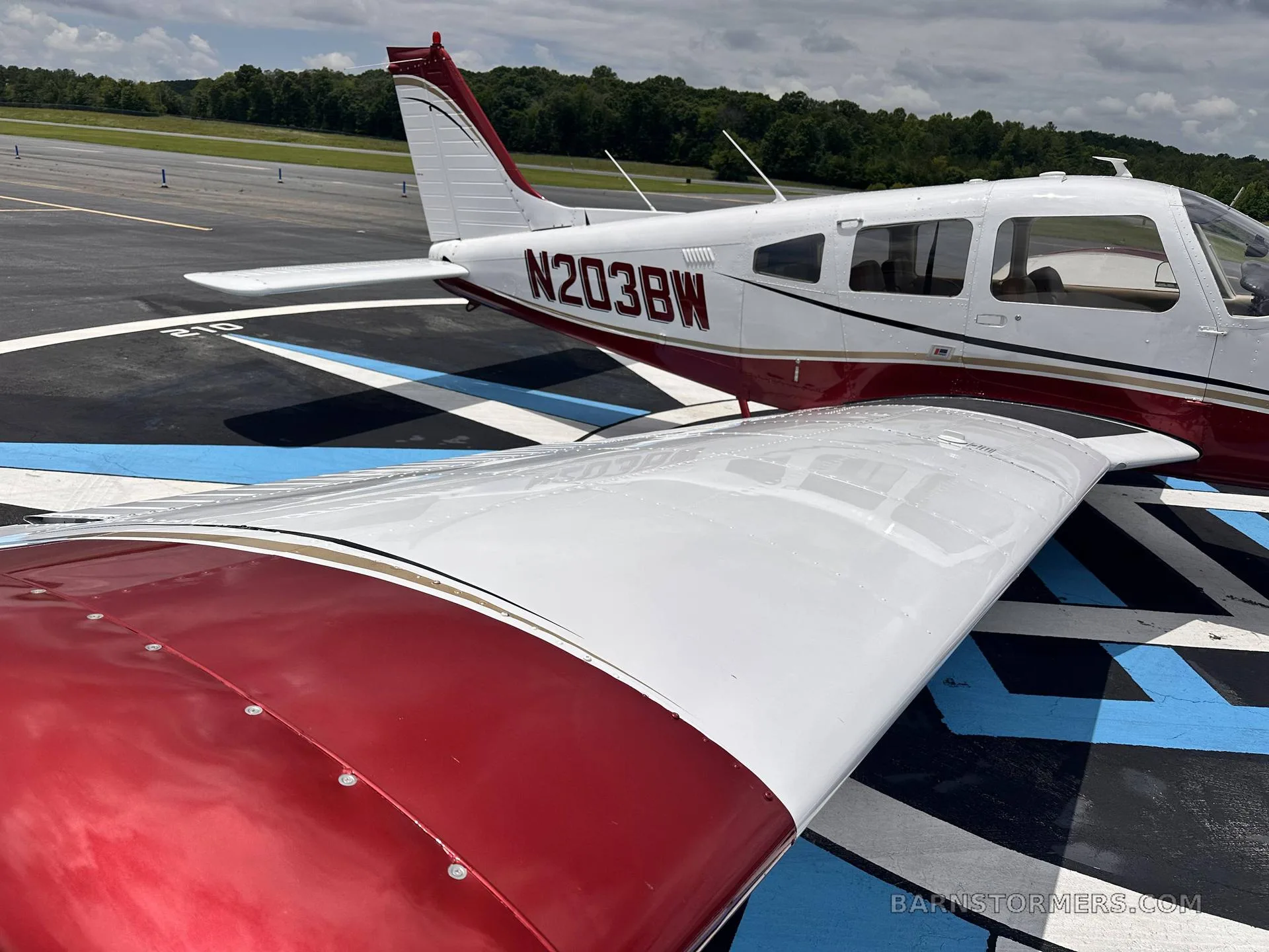 A close-up view of the white and maroon single-engine propeller aircraft (N203BW) showing the wing and tail on a patterned tarmac.