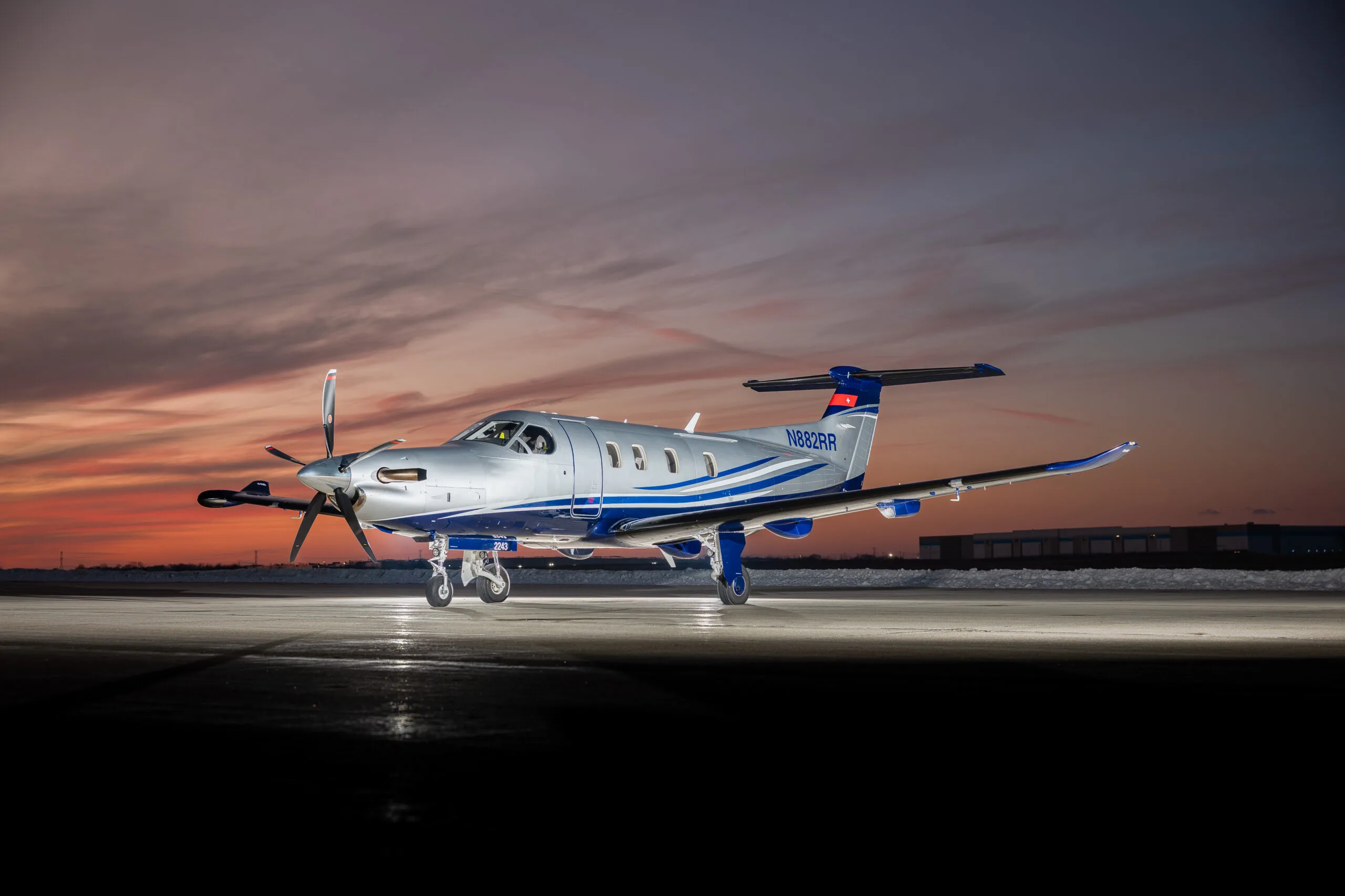 A silver and blue Pilatus PC-12 aircraft with tail number N882RR is parked on a tarmac at sunset.