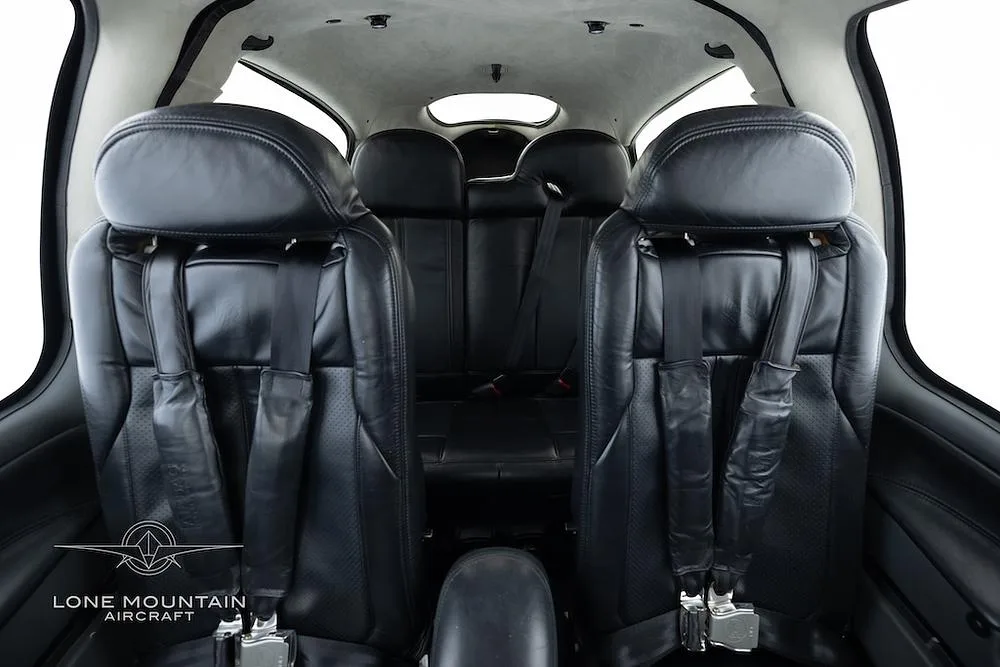 The black leather interior of a Cirrus SR22 aircraft, showing two front seats and two rear seats with seatbelts.