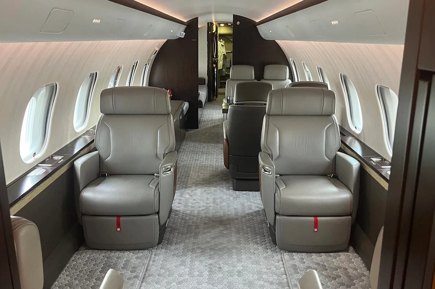 The luxurious cabin interior of a business jet with grey leather seats and a patterned carpet.