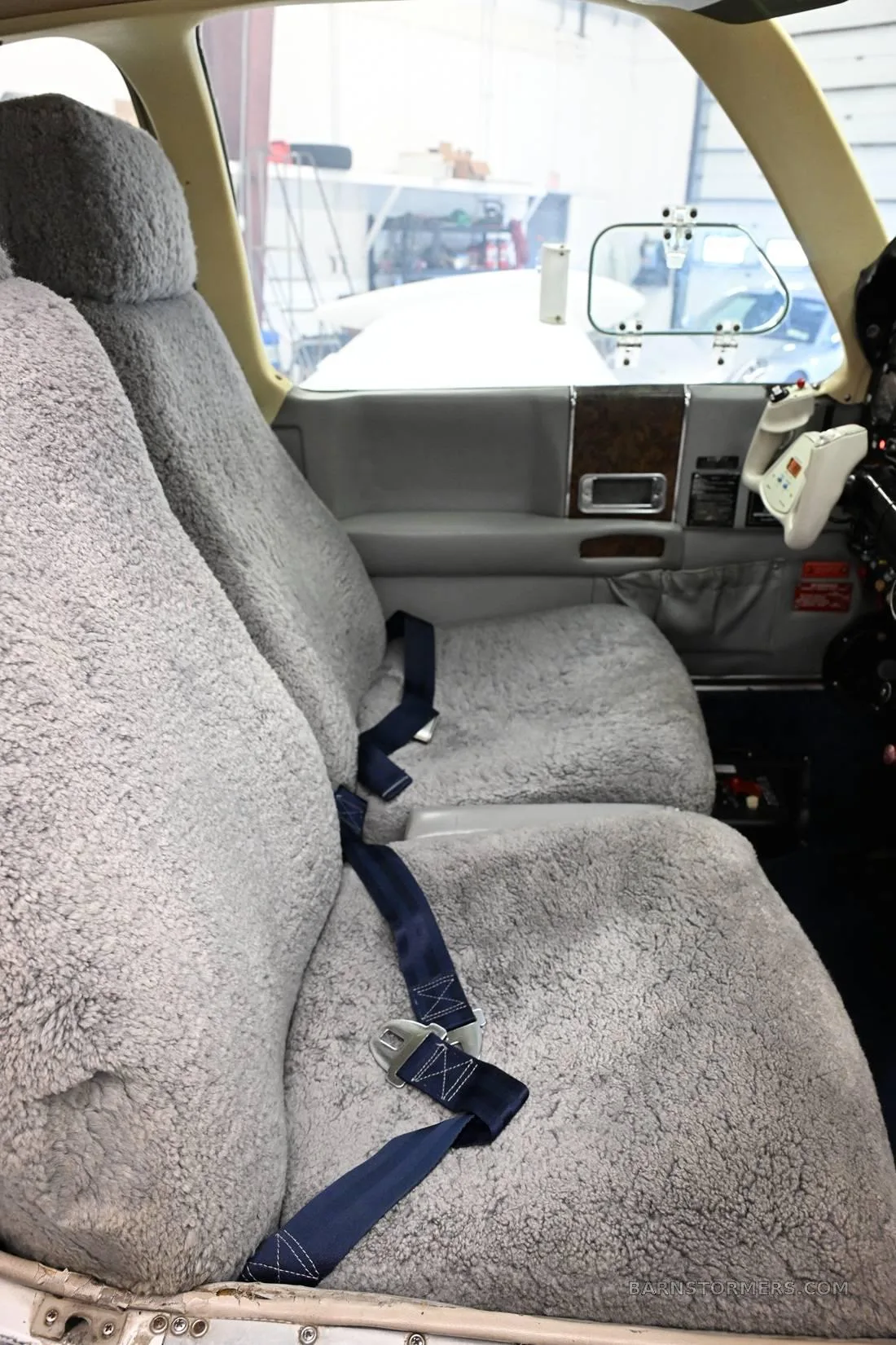 The interior of an aircraft cabin showing two grey sheepskin-covered seats with blue seatbelts.