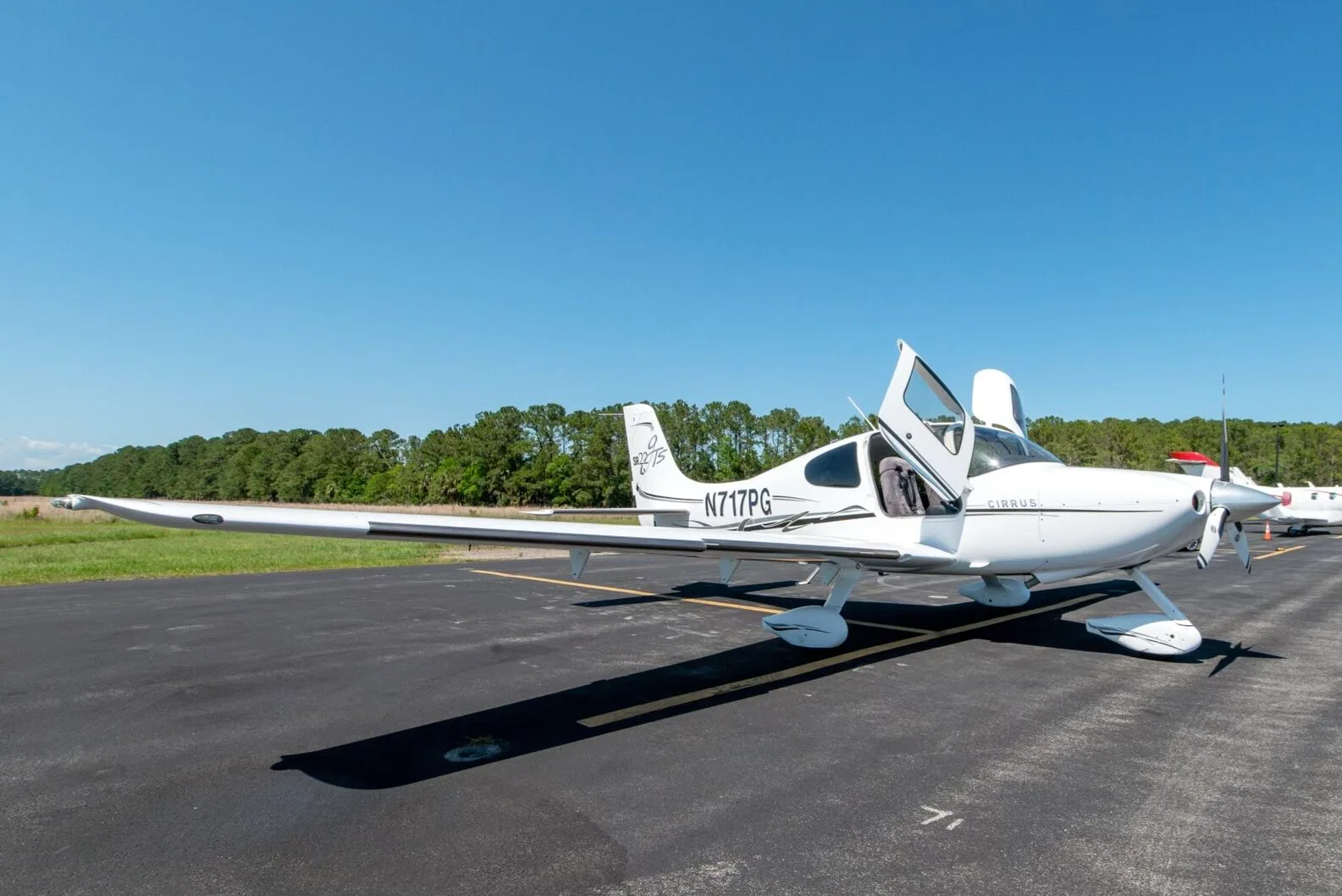 White Cirrus SR22T aircraft N717PG with black and grey stripes and open doors parked on an airfield.