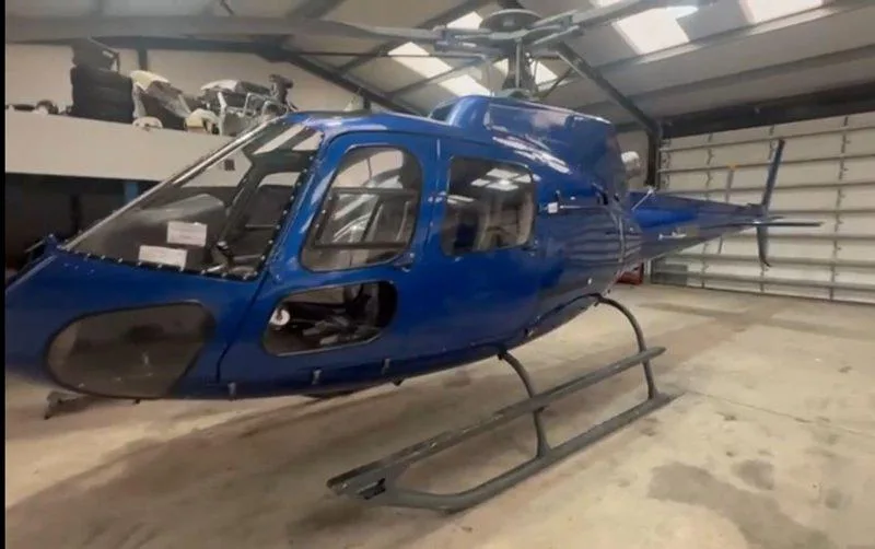 A blue helicopter, possibly an Airbus H125, in a hangar, appearing to be under maintenance.