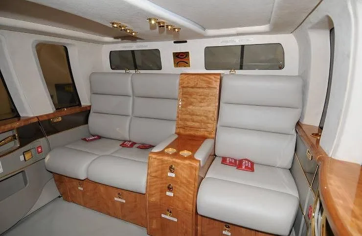 A luxurious helicopter interior with light gray leather seats, wood paneling, and gold accents.
