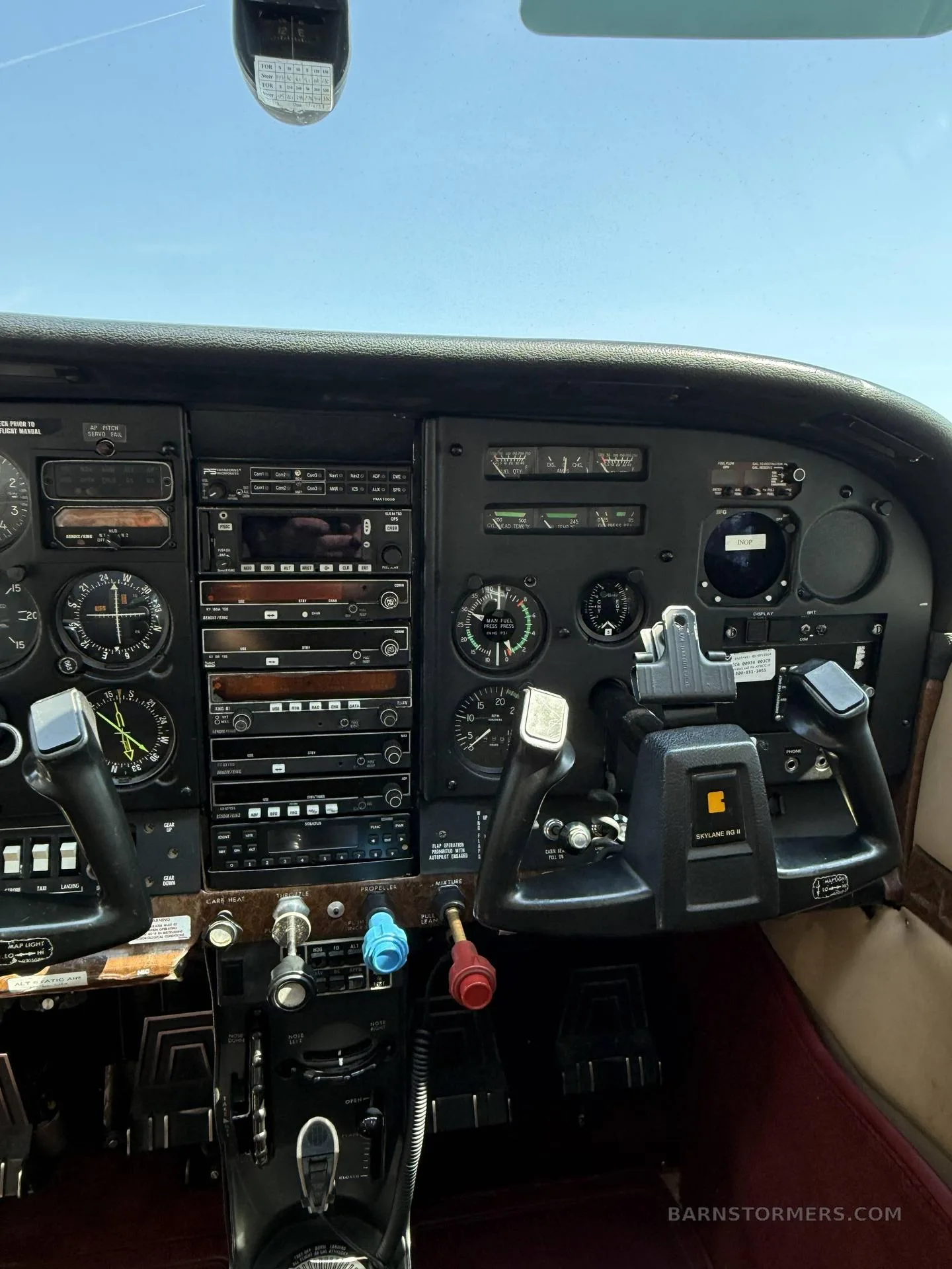 A wide view of a light aircraft cockpit, showing the full instrument panel, both control yokes, and a clear sky through the windshield.