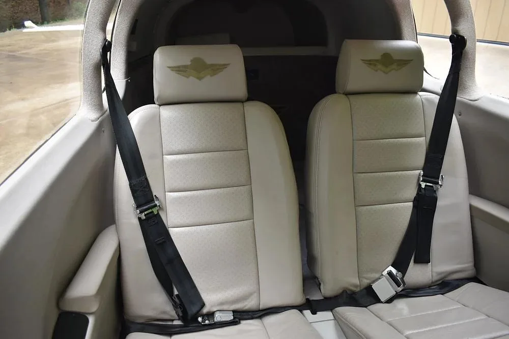 The front two light-colored leather seats with seatbelts in the aircraft cabin, each headrest featuring a gold winged logo.
