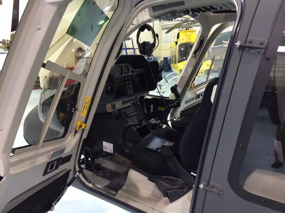 The cockpit of a helicopter viewed through an open door, showing the instrument panel and pilot's seat.