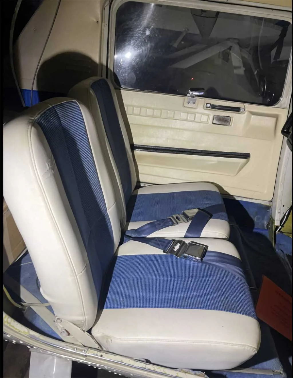 The interior of an aircraft cabin shows two white and blue upholstered seats with seatbelts.