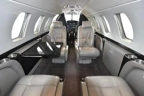 The luxurious interior cabin of a business jet with light grey leather seats and a dark wood floor.