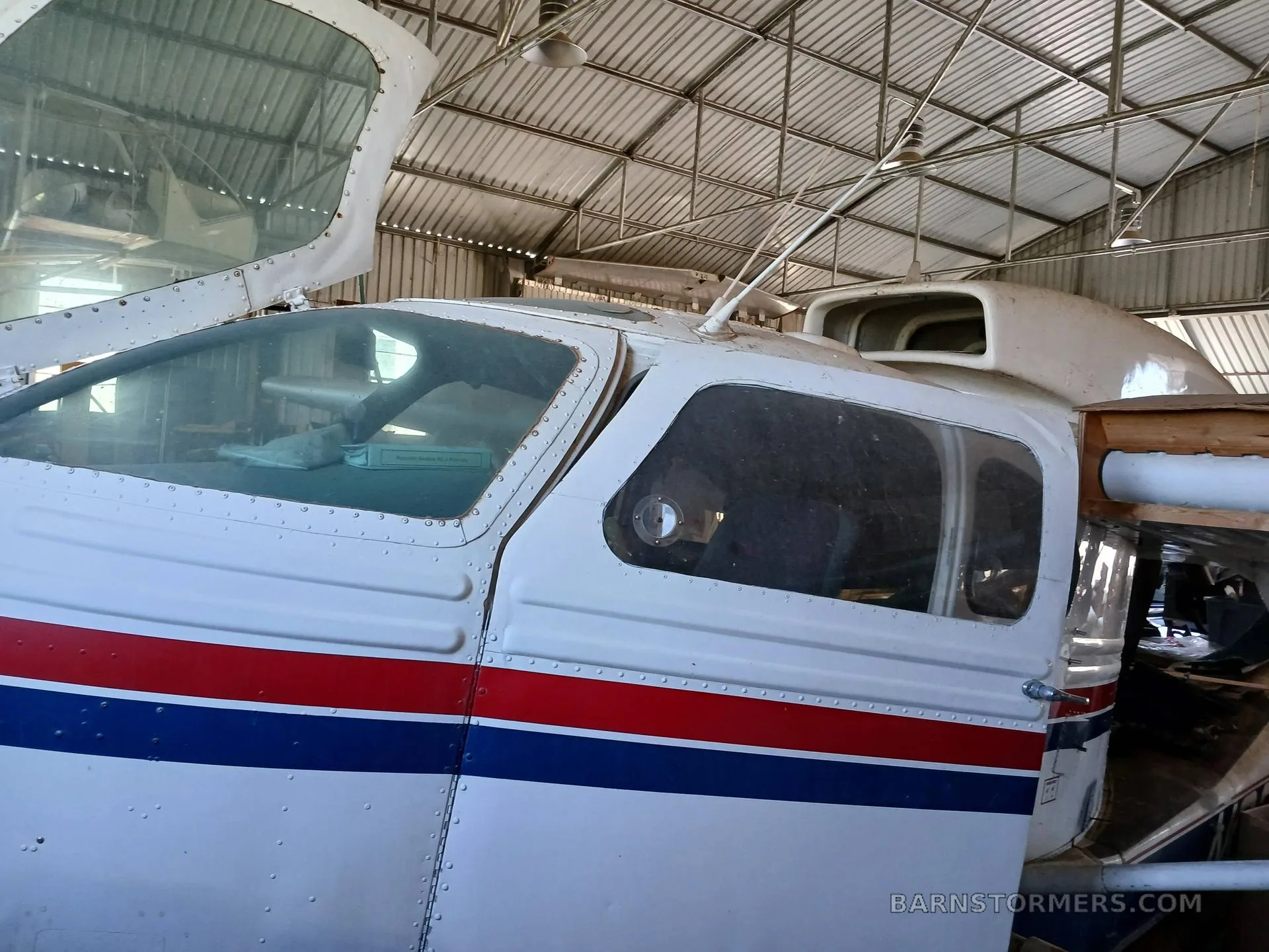 Close-up view of the cockpit and front fuselage of a white, red, and blue amphibious aircraft inside a hangar.