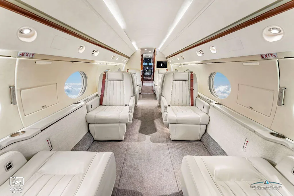 The luxurious cabin interior of a Gulfstream G550, featuring light-colored leather seats and a spacious aisle.