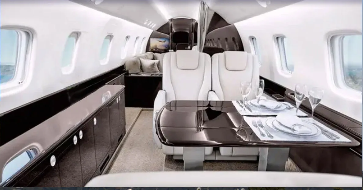 The luxurious interior of a private jet cabin features white leather seats, a set dining table, and dark wood accents.