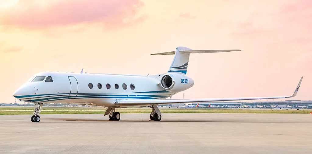 A Gulfstream G550 business jet with a white and blue livery, tail number N535V, parked on the tarmac at sunset.