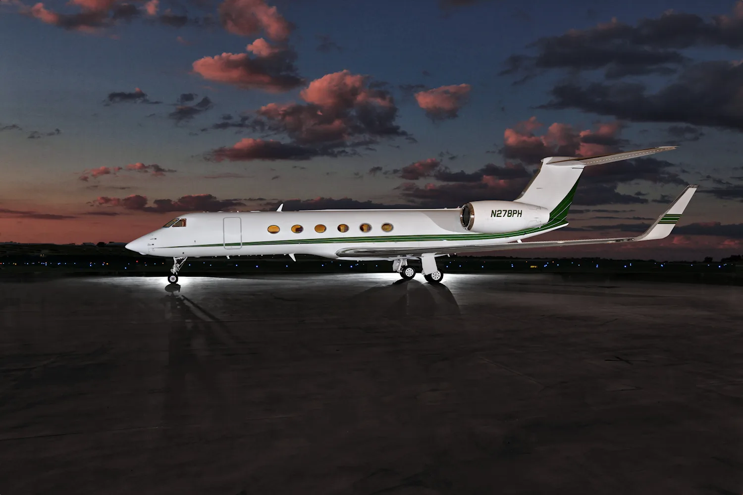 A white Gulfstream business jet with a green stripe, registration N278BPH, parked on a reflective tarmac at dusk.