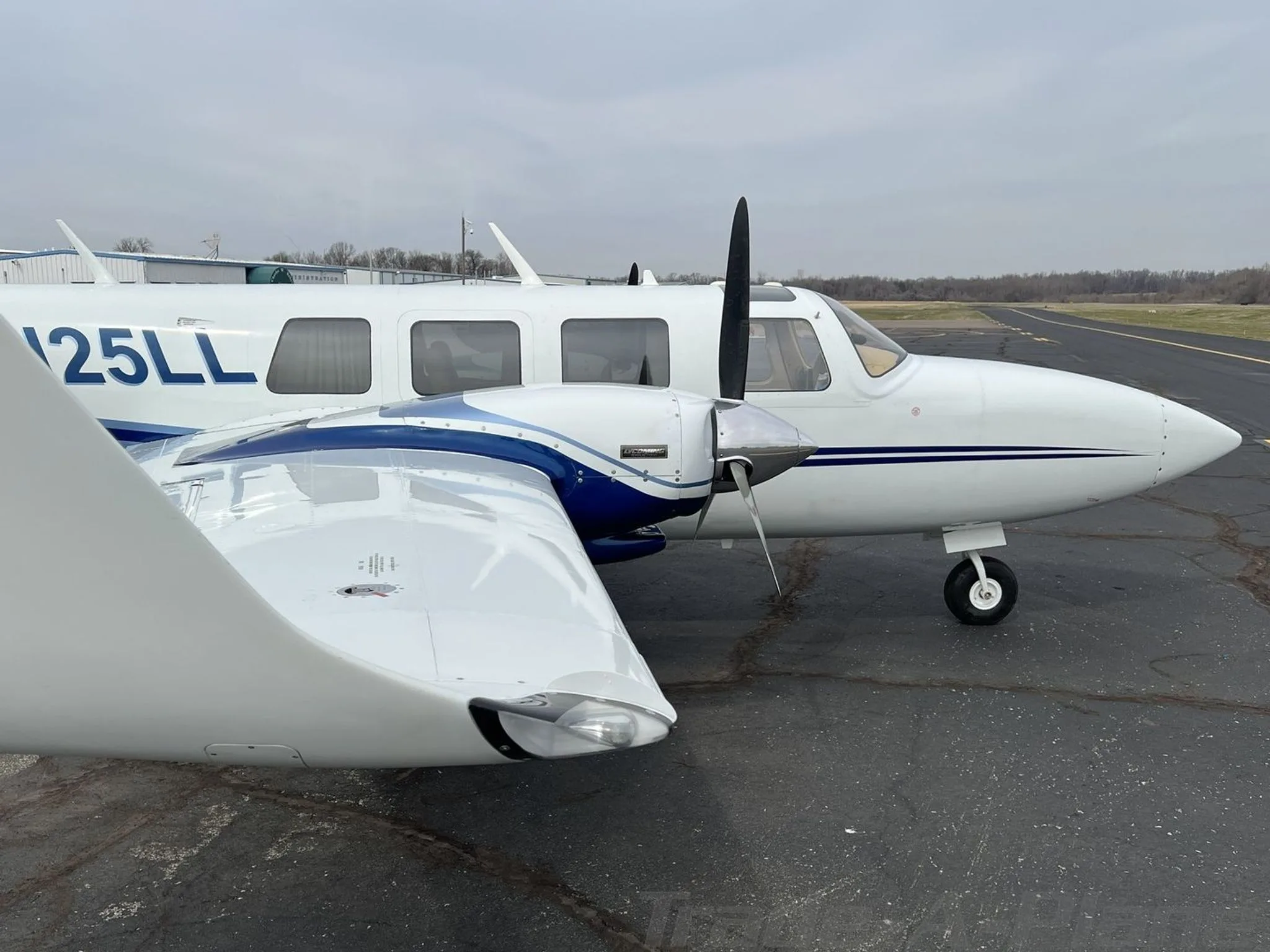 Side view of the cockpit and wing of the N25LL aircraft, showing the propeller and blue stripe.