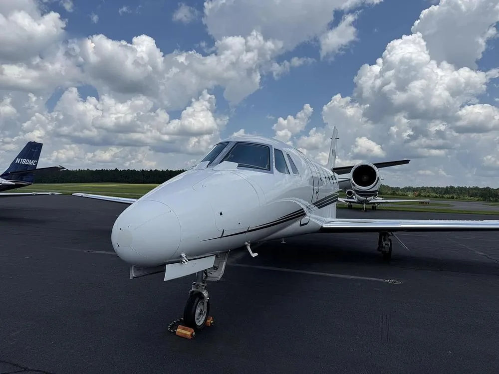 A front-quarter view of a white Cessna Citation private jet with black and grey stripes parked on an airport tarmac.