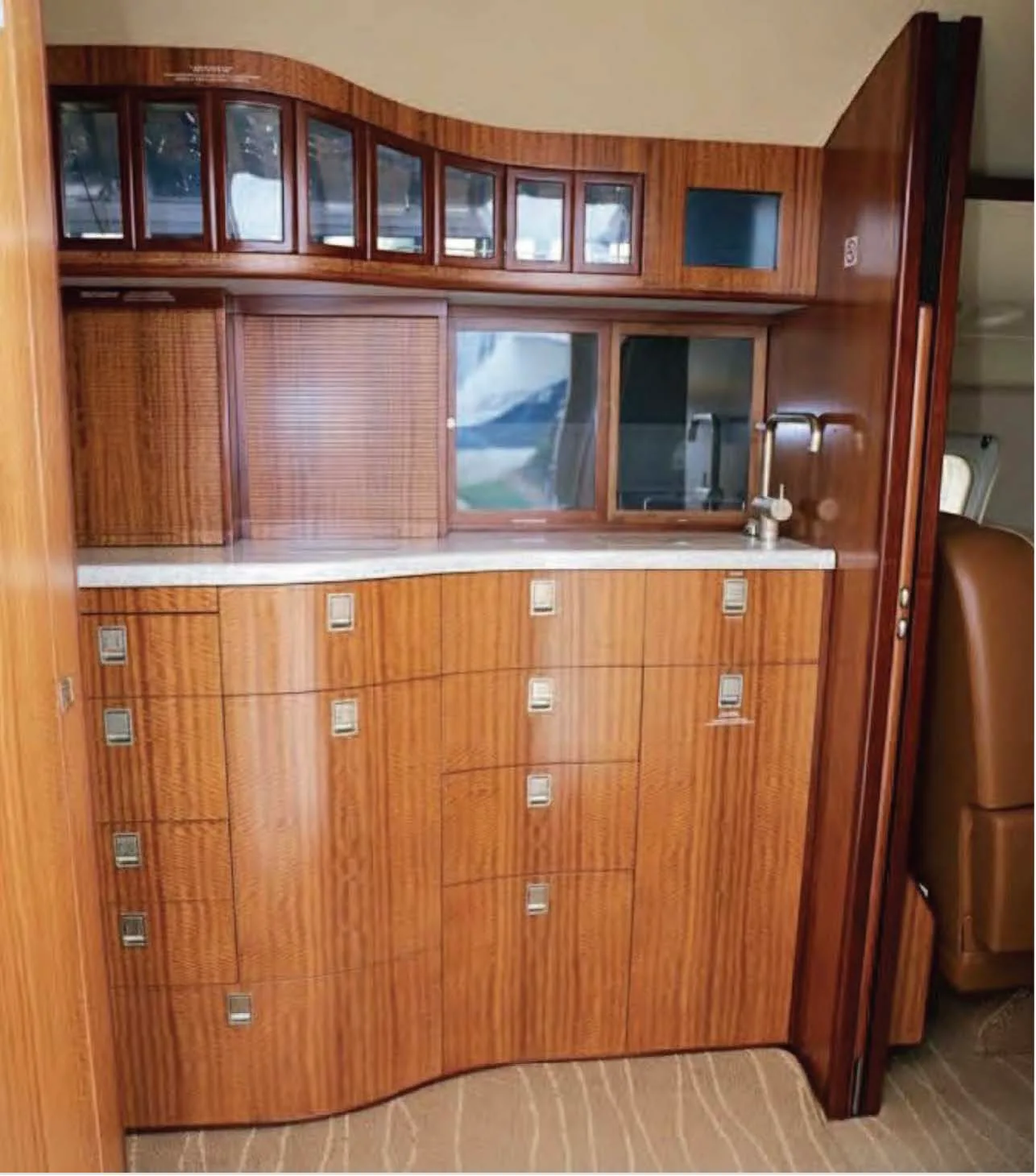 A luxurious aircraft galley with wooden cabinetry, a countertop, and a small sink.