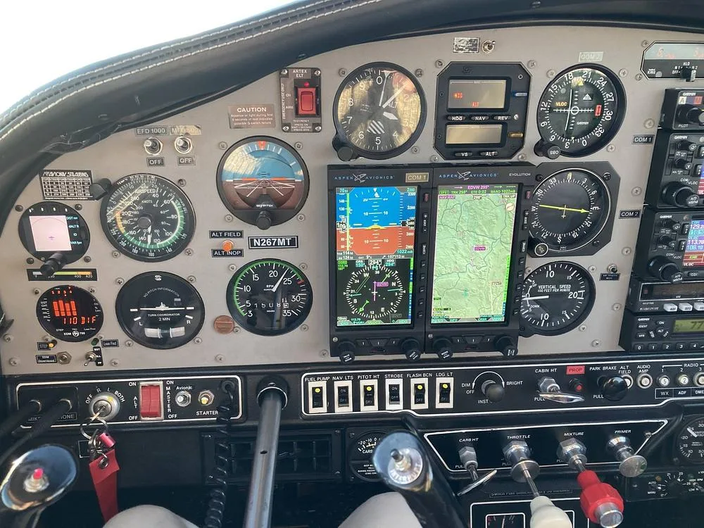 A close-up of the left side of the Grumman American AA-5B Tiger's cockpit panel, featuring traditional gauges and modern avionics displays.