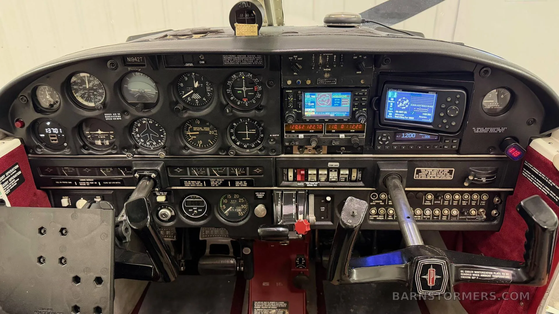 The cockpit instrument panel of a small aircraft, featuring analog gauges, a Garmin GPS, and a control yoke with an Oldsmobile logo.