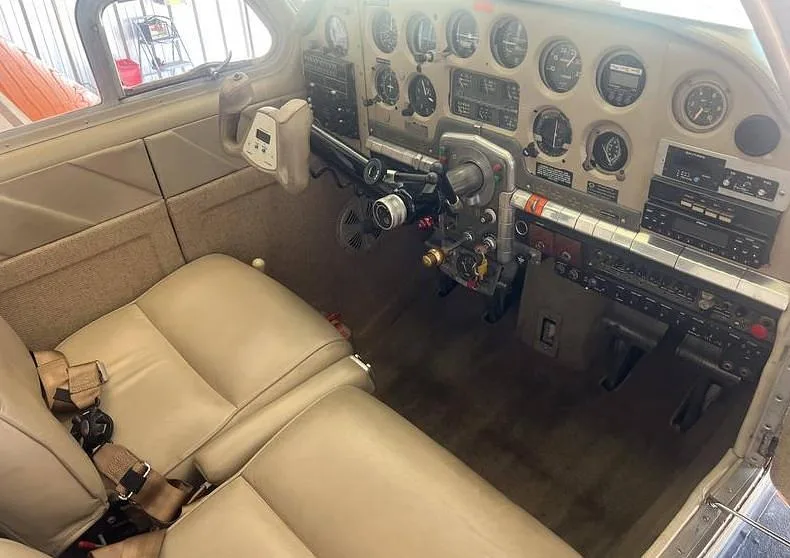 The cockpit of a Beechcraft Bonanza showing the instrument panel, yokes, and tan leather front seats.