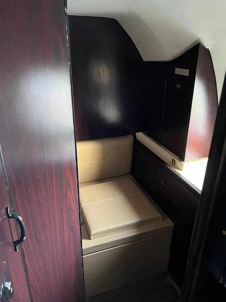 A small tan upholstered seat in a private section of the aircraft cabin with dark wood paneling.