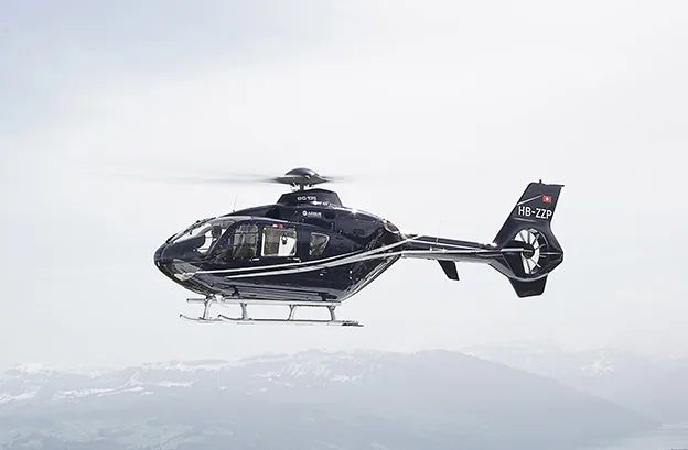 An Airbus EC135 helicopter in flight over a mountainous landscape.