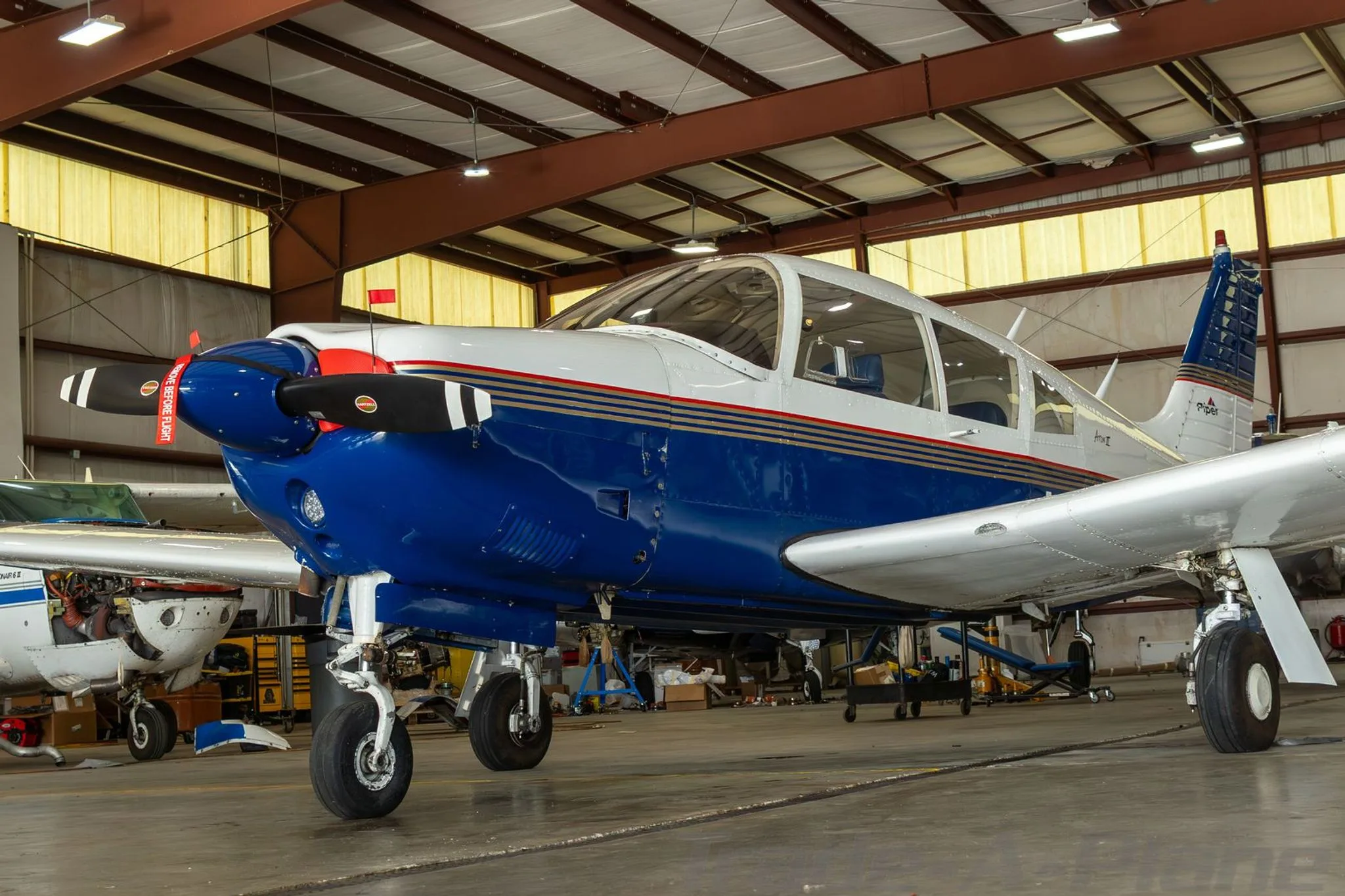 A Piper Arrow II aircraft with a blue and white paint scheme, parked inside a hangar.