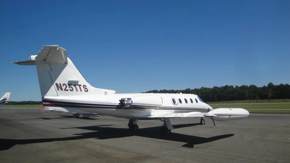 A white Learjet N251TS is parked on an airport tarmac, viewed from the rear-left side.