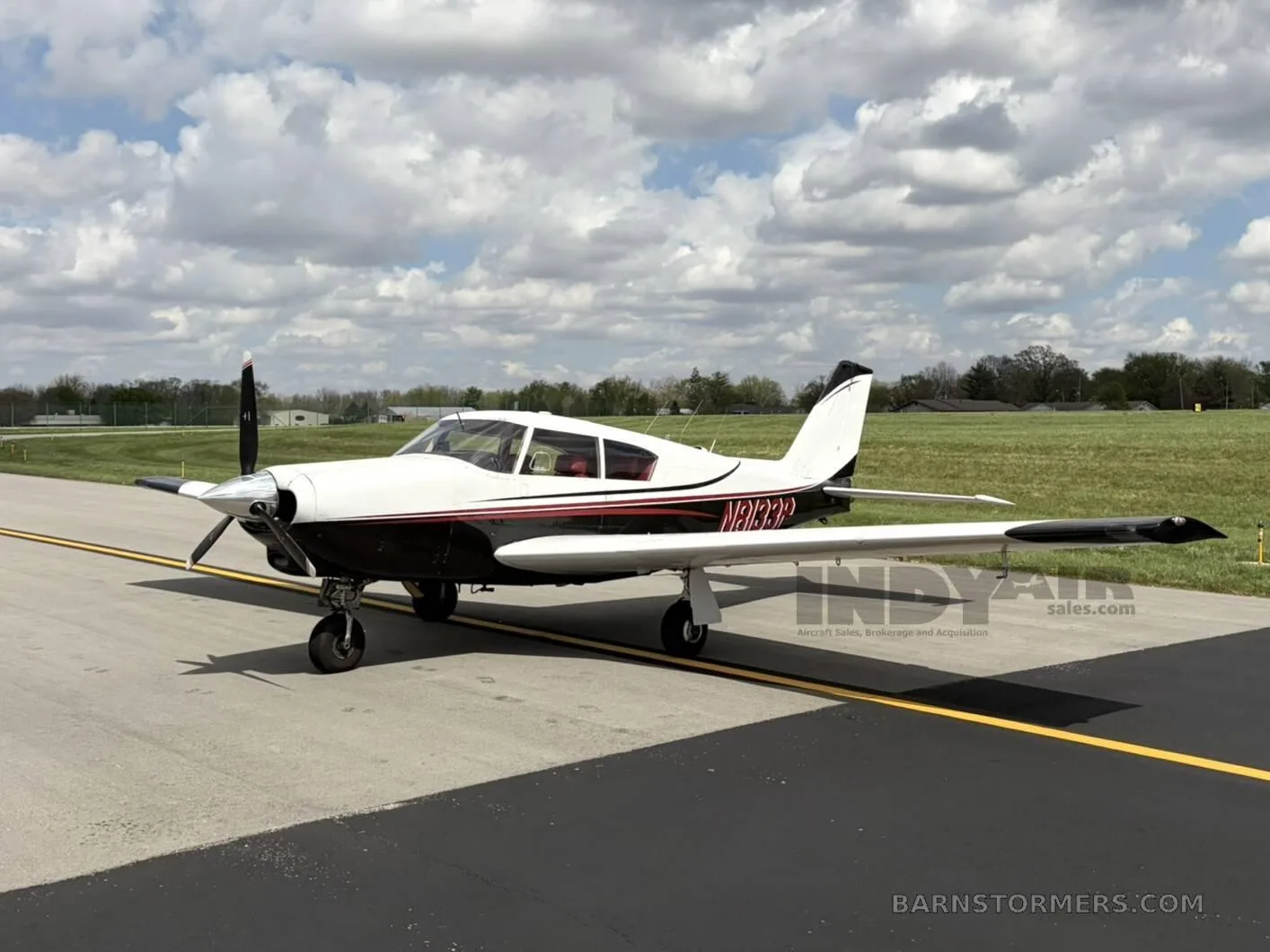 A white and black single-engine propeller aircraft with red accents, viewed from the front-left, parked on an asphalt taxiway.
