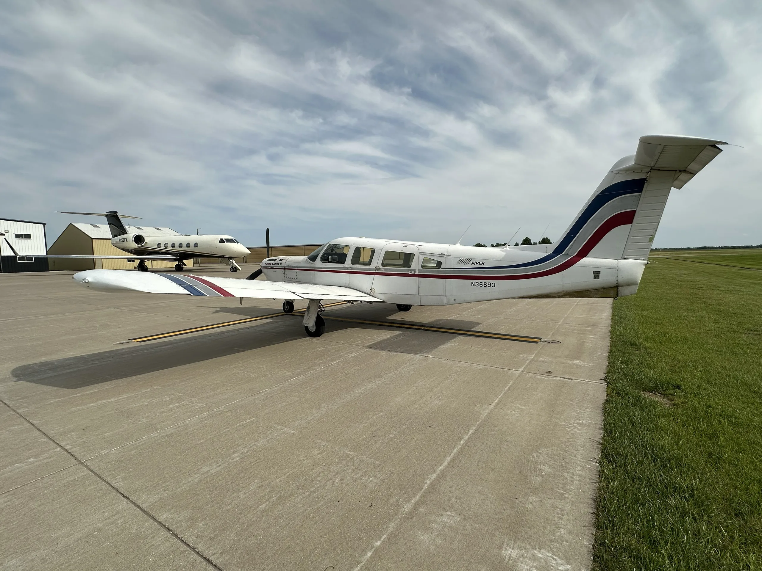 A white Piper Turbo Lance II aircraft, N36693, parked on an airfield with a private jet in the background.