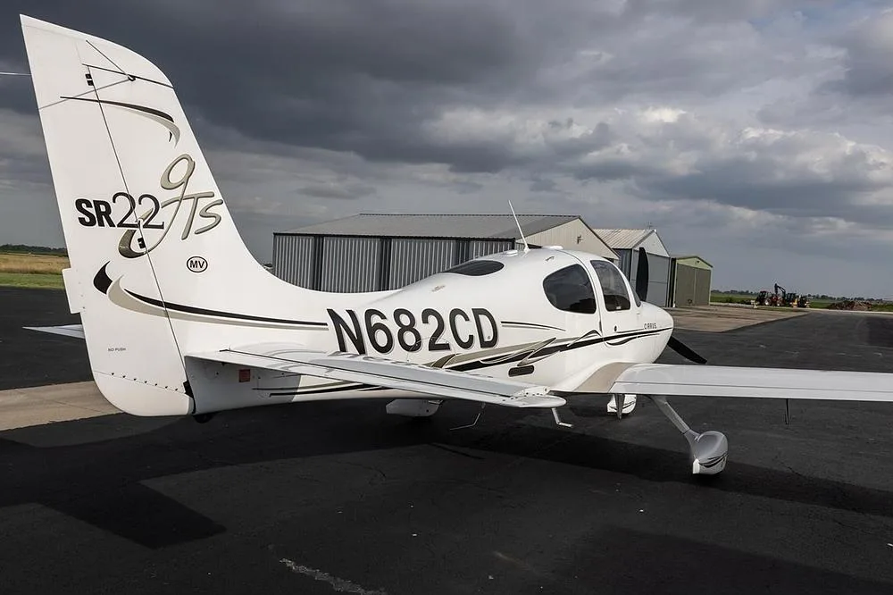 A rear-right view of a white Cirrus SR22T aircraft with black and gold accents, registration N682CD, parked on an airfield.