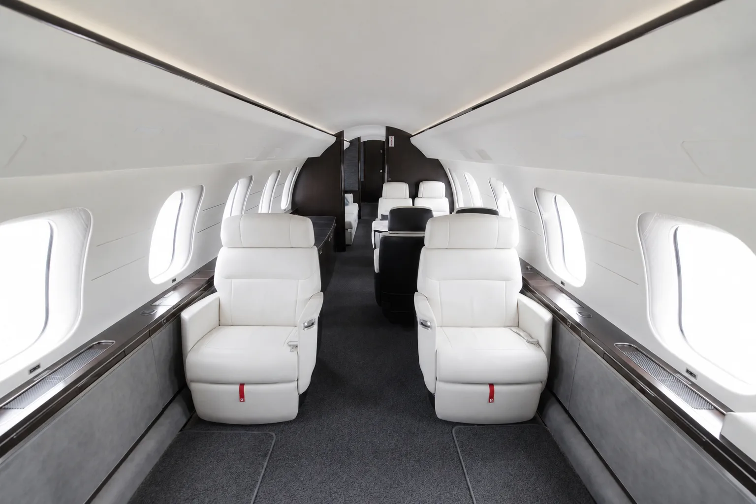 The spacious main cabin of a private jet, featuring rows of white leather seats and large windows.
