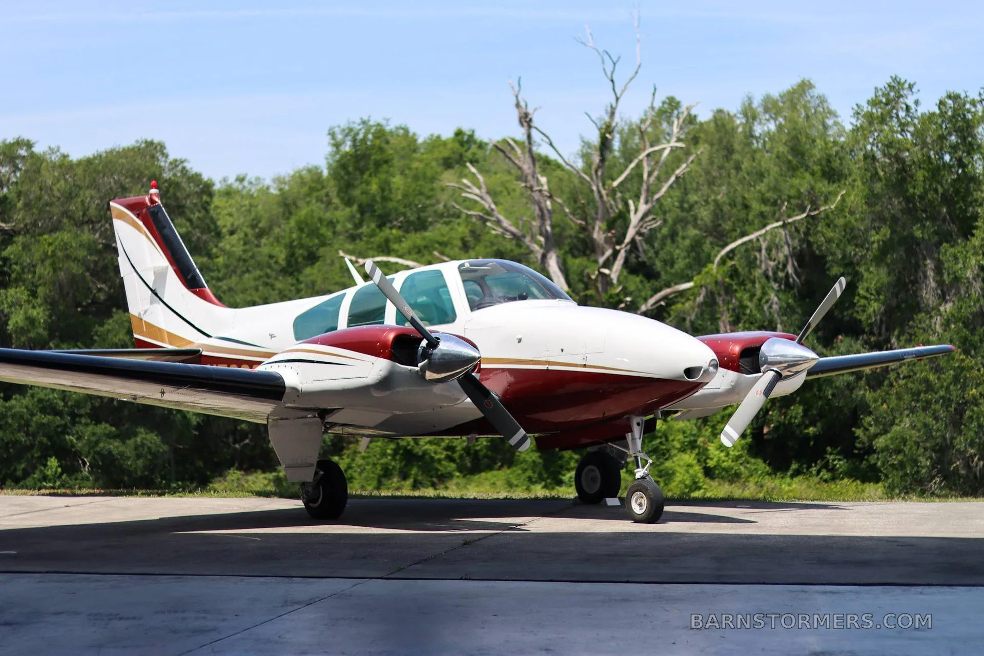 A white and maroon twin-engine propeller aircraft with gold stripes is parked on a tarmac, viewed from a slightly different angle.