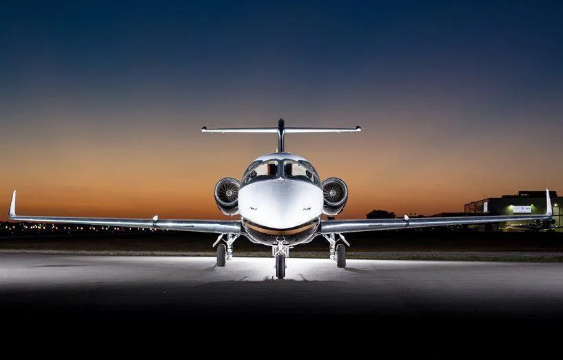 A Learjet 400XP with a black and white paint scheme, viewed from the front, parked on a tarmac at sunset.