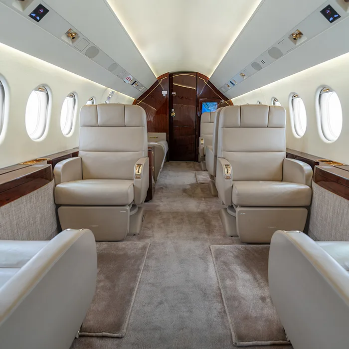 A view down the aisle of the aircraft cabin, showing leather seats and wood trim.