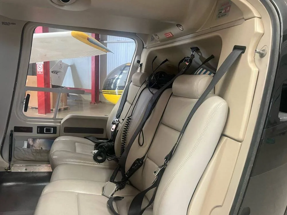 The beige passenger seats and interior cabin of a helicopter, with another aircraft visible outside.