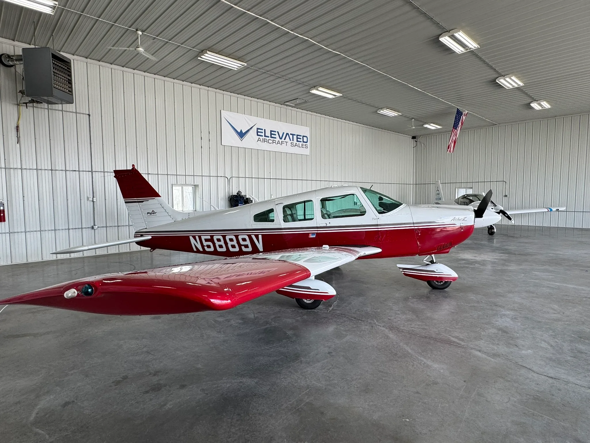 A red and white Piper Cherokee aircraft, tail number N5889V, parked inside a hangar.