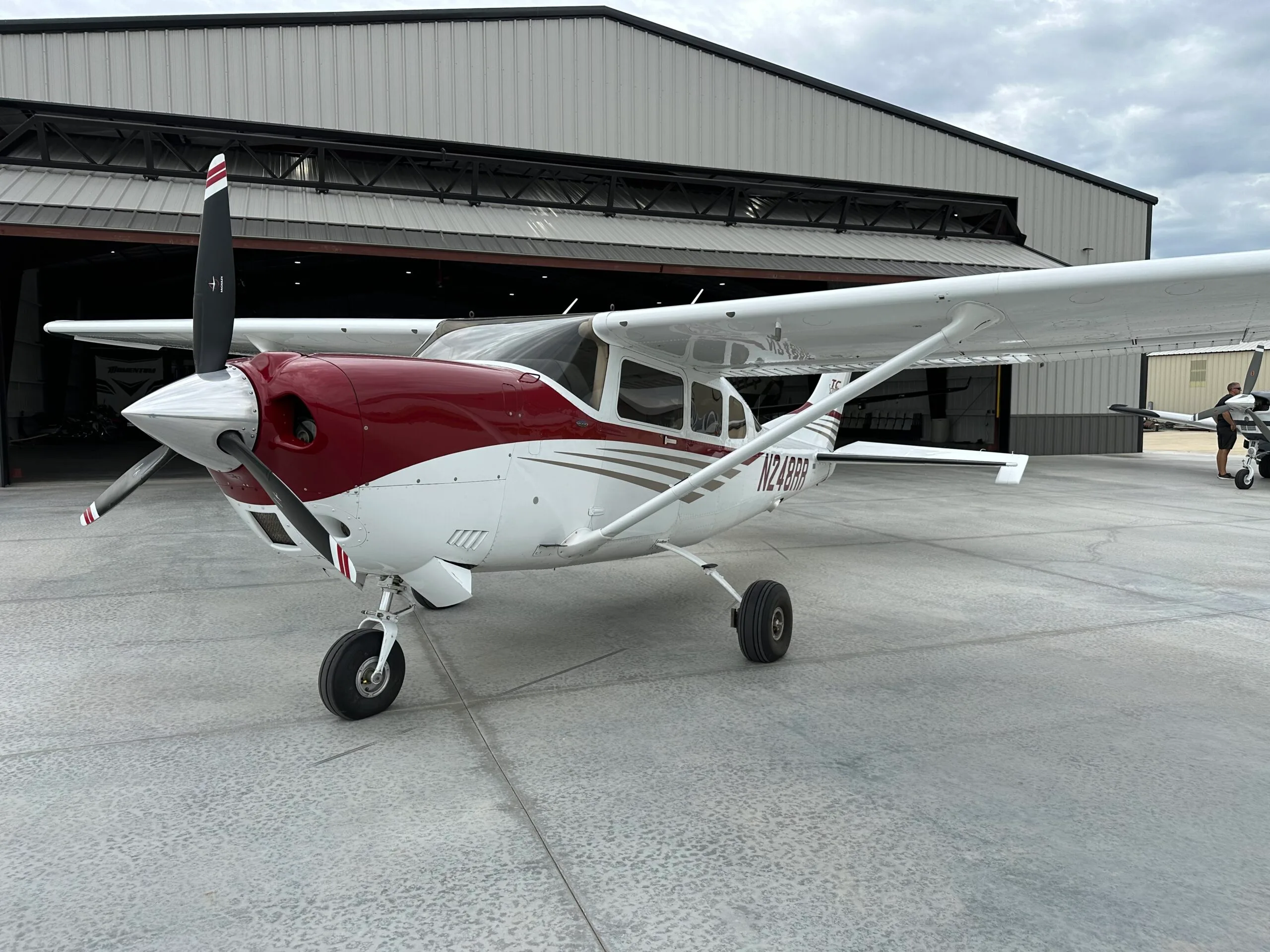 A white and red single-engine propeller aircraft, registration N248RR, parked on an airport apron in front of a hangar.