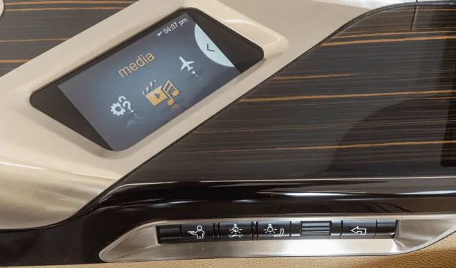 A close-up of a private jet's cabin control panel with a media screen and buttons for lighting and other functions.