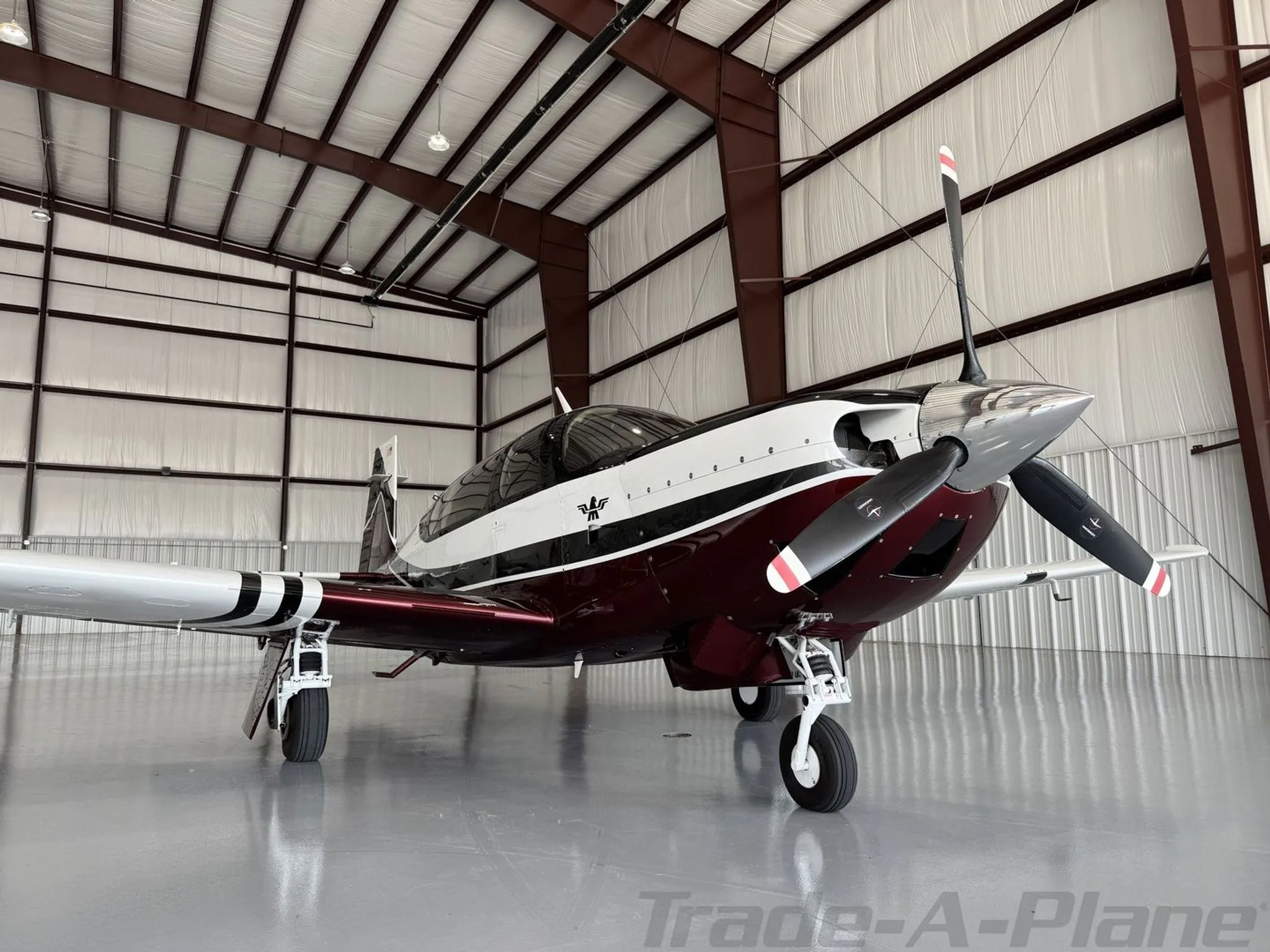 A Mooney aircraft with a maroon, white, and black paint scheme is parked in a hangar, viewed from the front right.